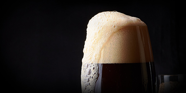 Dark beer with foaming overflowing from the rim