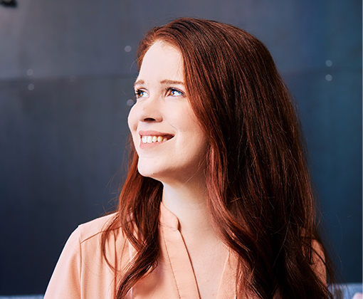 alyssa reynolds - woman with red hair and a pink blouse smiling looking in an eastern exposure against a navy blue background