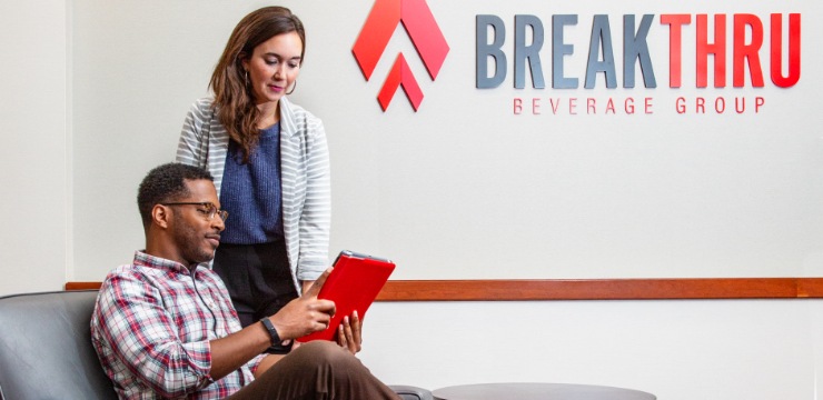 man sitting in a chair reviews a tablet device with a woman standing besides him