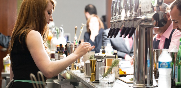 female mixologist adds an herb garnish to a freshly finished cocktail on a bar