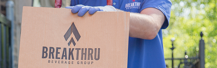 blue gloved hand resting on a cardboard packaging box with a Breakthru Beverage Group logo