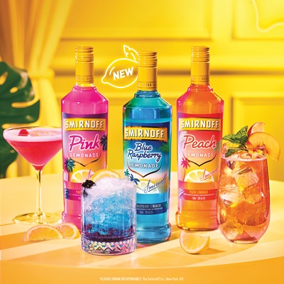 Three bottles of Smirnoff Vodka sitting on a table surrounded by cocktails. The wall in the back is yellow and a palm leaf can be seen