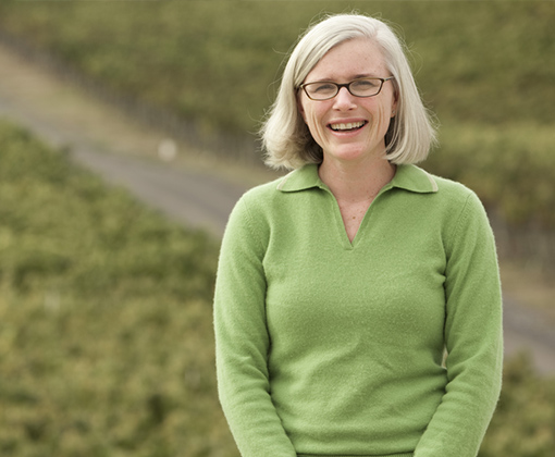 blonde hair woman with glasses wearing a green sweater standing in a vineyard