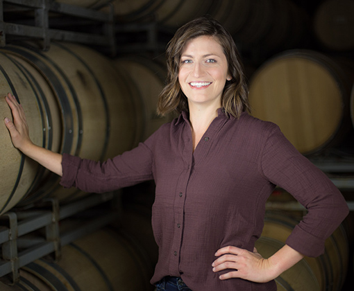 pale skin brunette woman with maroon shirt in a room of stacked barrels