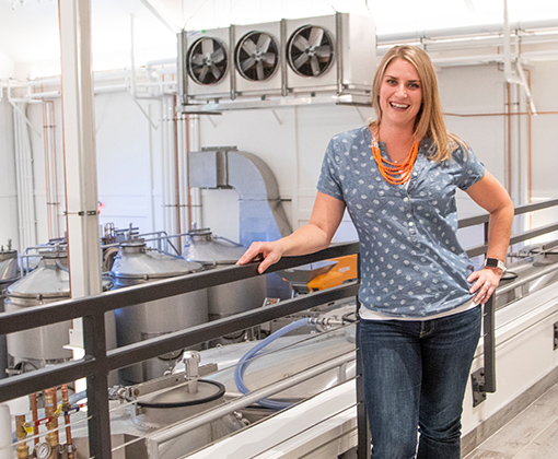 smiling blonde-haired woman in a blue polka dot shirt standing in a warehouse