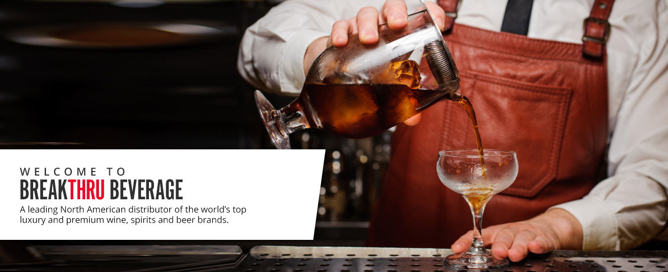 man in brown leather apron pouring brown iced liquor from a strained mixing glass into a coupe glass on a bartop