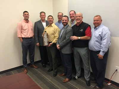 Eight men posing for a photo with a personalized bottle of Bols Genever